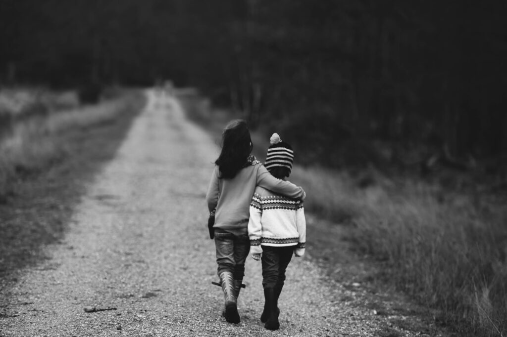 black and white image of a young sister with hand over little brother's shoulder, walking along a dirt road