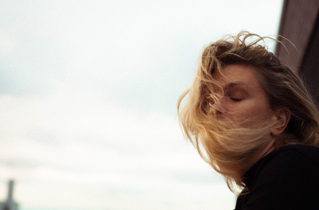 side profile of a blonde woman against the sunlight with the hair blowing to her face representing the article "What's Mine is Mine and What's Yours is Mine" by Comfortable Hell