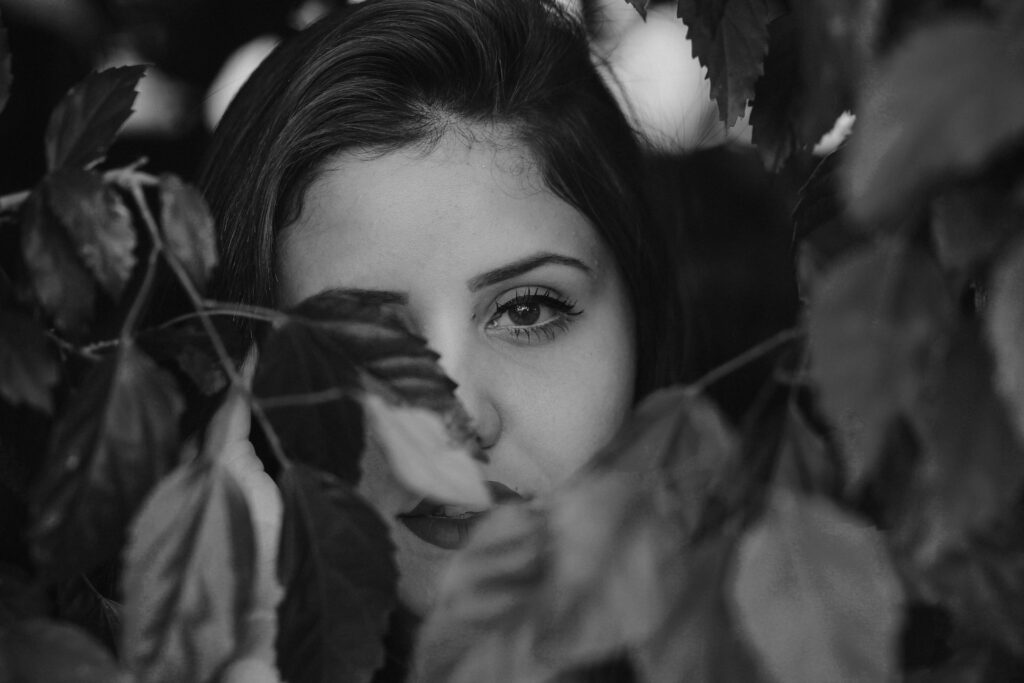 a closeup image of a woman peaking through branches of leaves