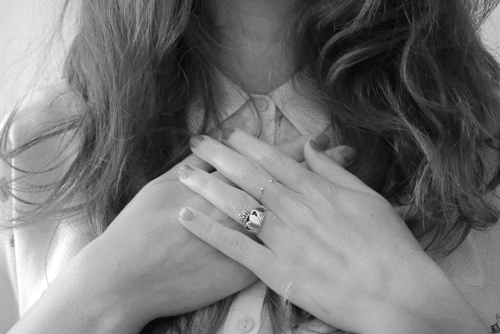 black and white closeup image of a woman with her hands to her chest, representing the article "Life Is a Team Effort, So Is Healing From Trauma" by Comfortable Hell