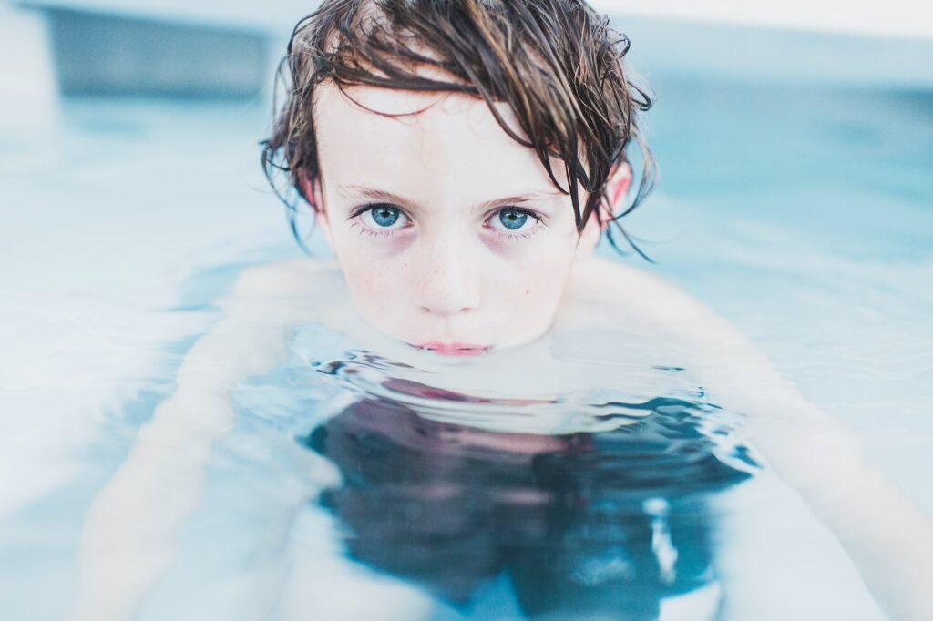 young boy in the pool with part of his face above the water, looking straight into the camera