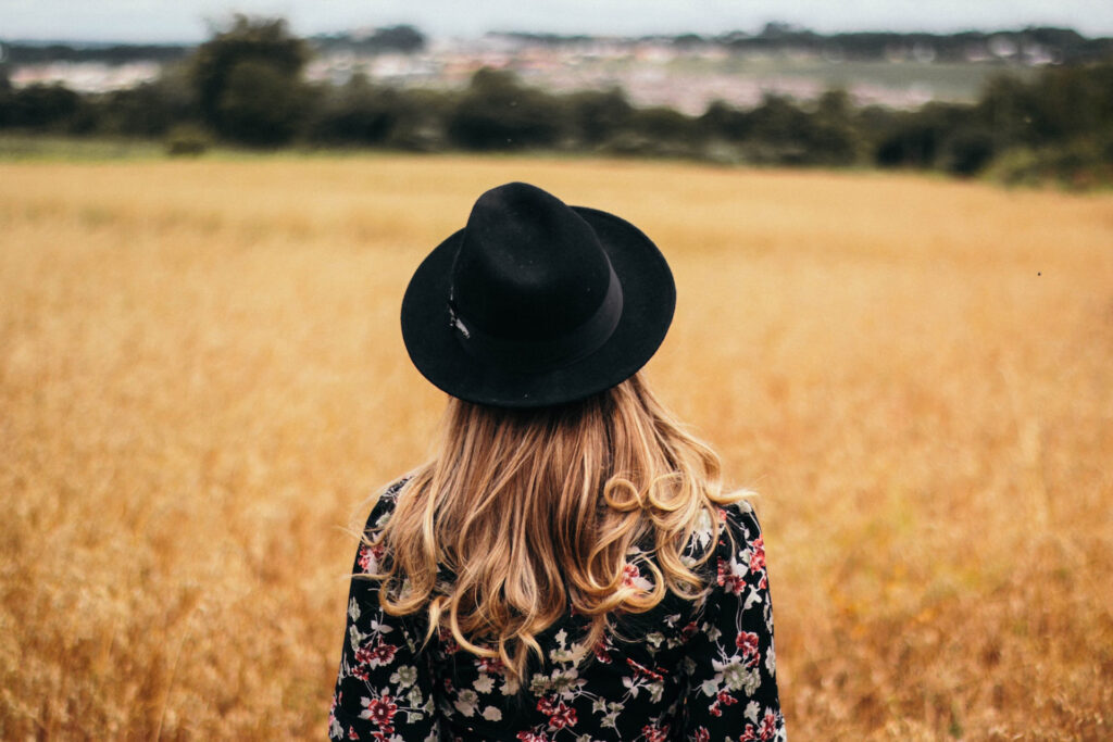 in an open field is a woman wearing a black hat with her back to the camera, representing the article "Tradeoffs Are Expensive" by Comfortable Hell